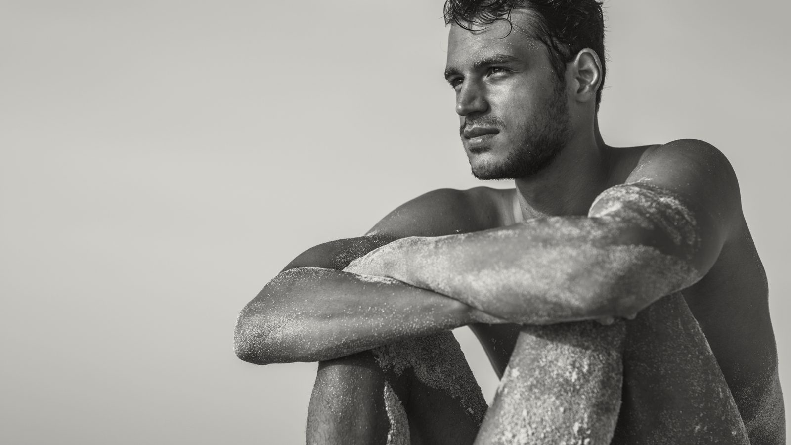 Muscular male creator sitting with his knees drawn up in black and white