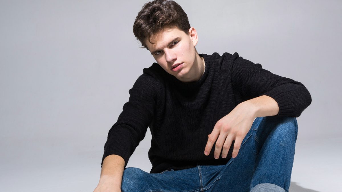 Male creator in a black sweater and jeans sitting against a grey background
