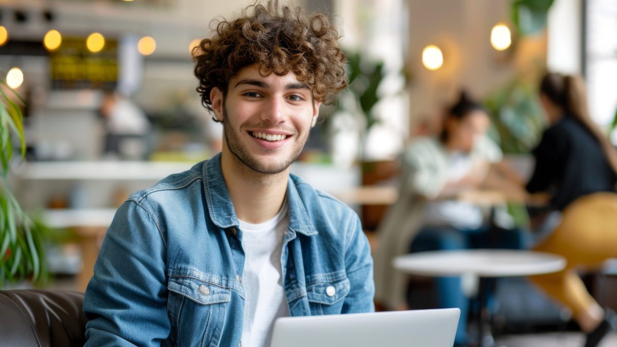 Male creator with curly hair working on a laptop in a cafe