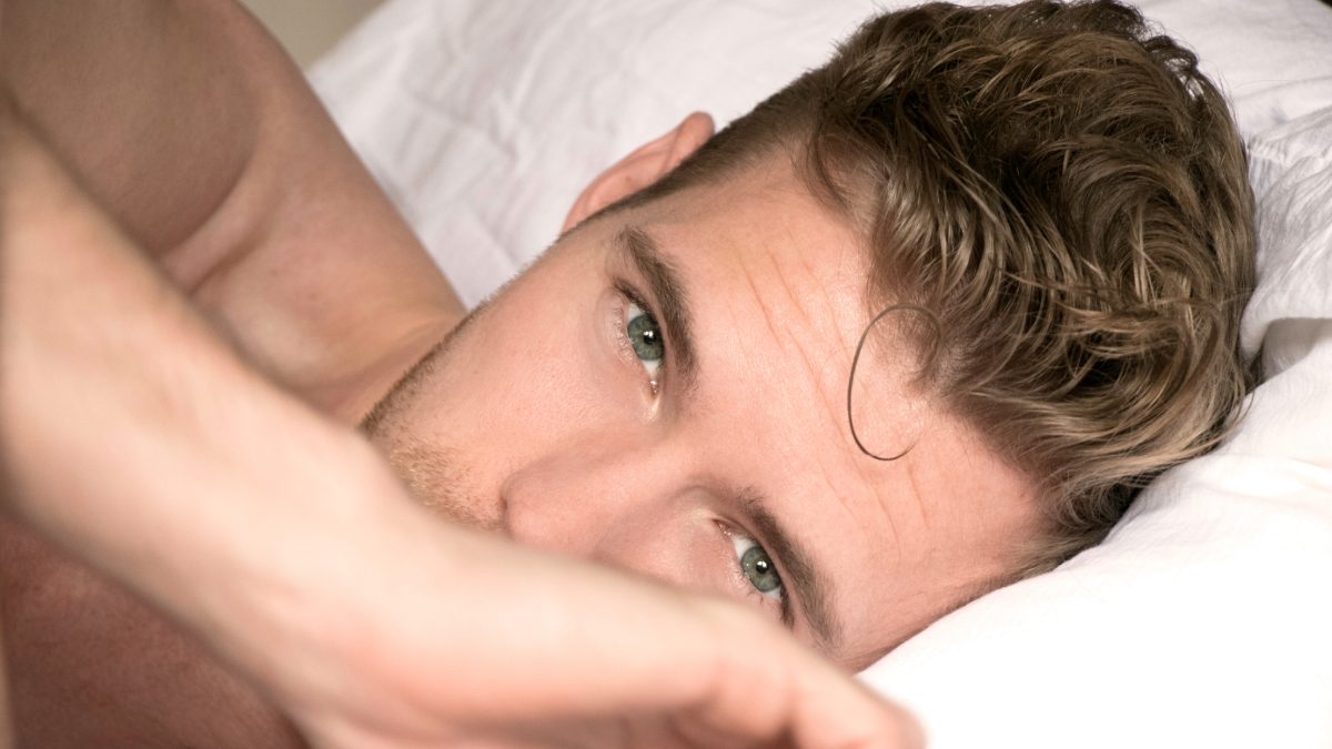 Male creator lying in bed looking at the camera
